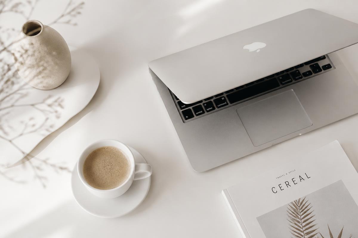 MacBook ouvert sur un bureau blanc épuré, tasse de café, lumière naturelle douce